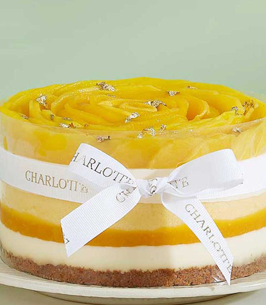 Exotic mango layer cake with creamy white mousse, dark crust, and golden mango rosette topped with edible glitter