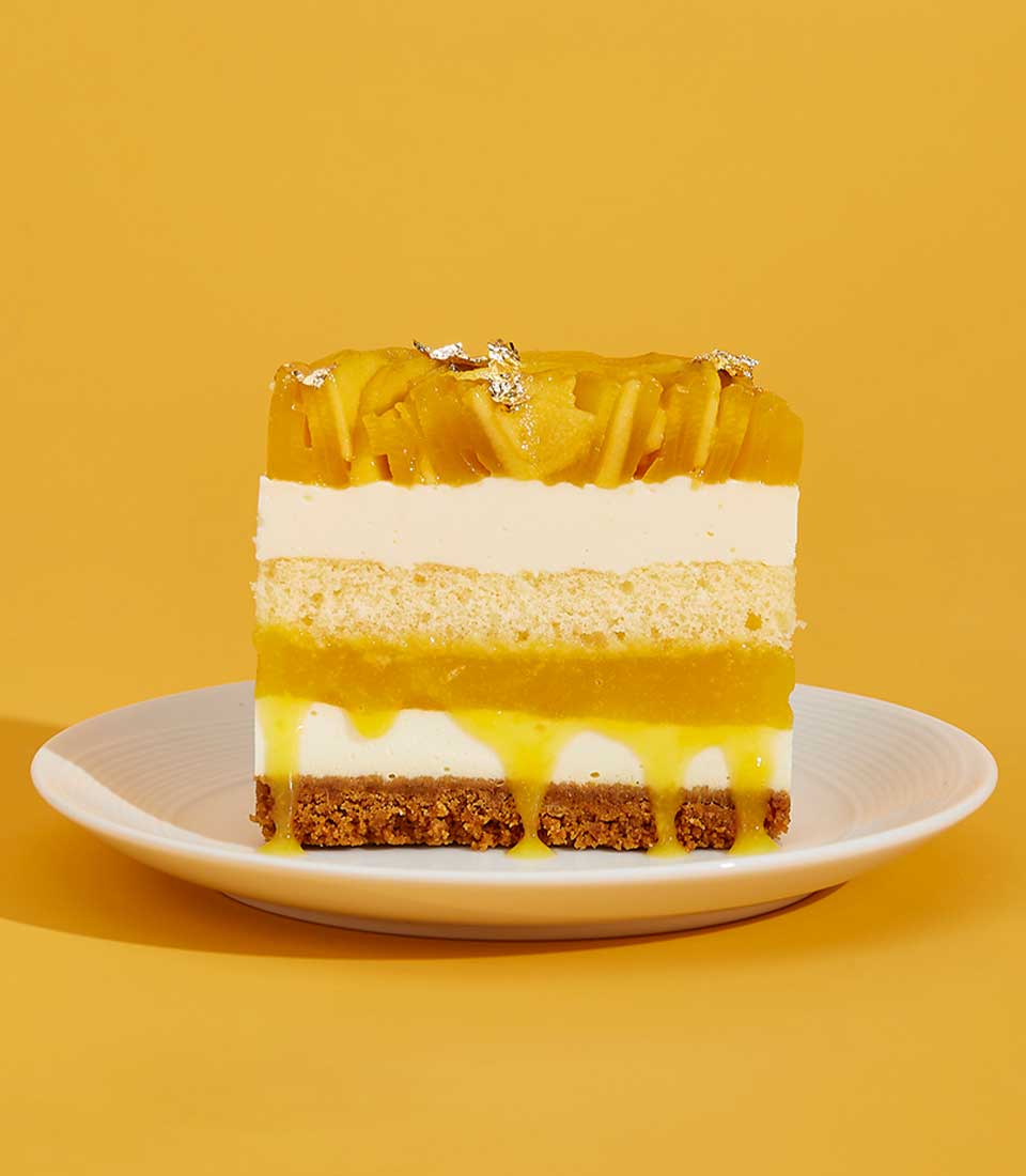 Vibrant multi-layered mango cake slice with cream, sponge, and fresh mango topped with edible silver leaf