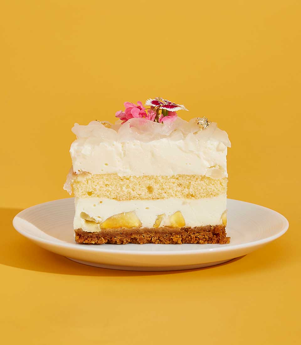 Layered creamy cake with banana, lychee, and gold leaf garnish on yellow background