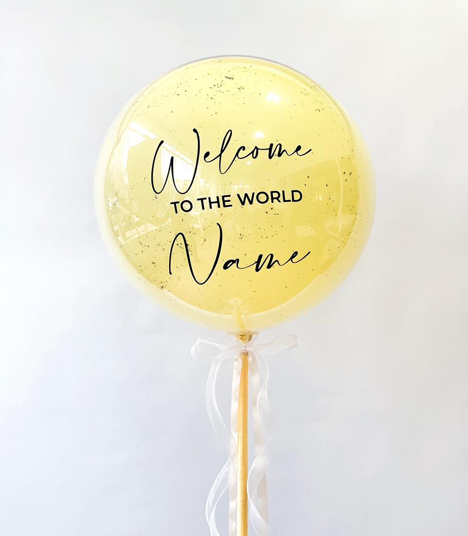 Golden shimmering "Welcome to the World" balloon gift with white ribbon bow on stick