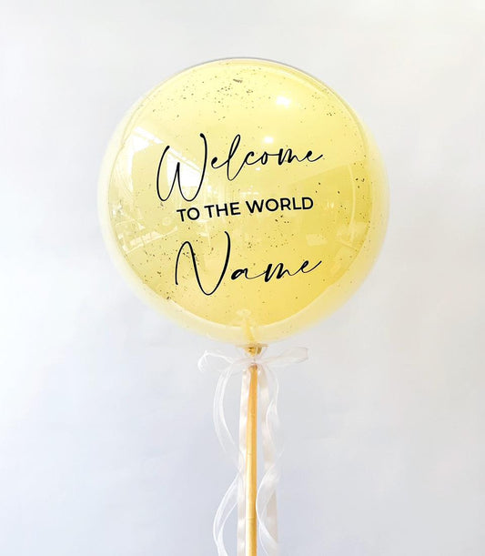 Golden shimmering "Welcome to the World" balloon gift with white ribbon bow on stick