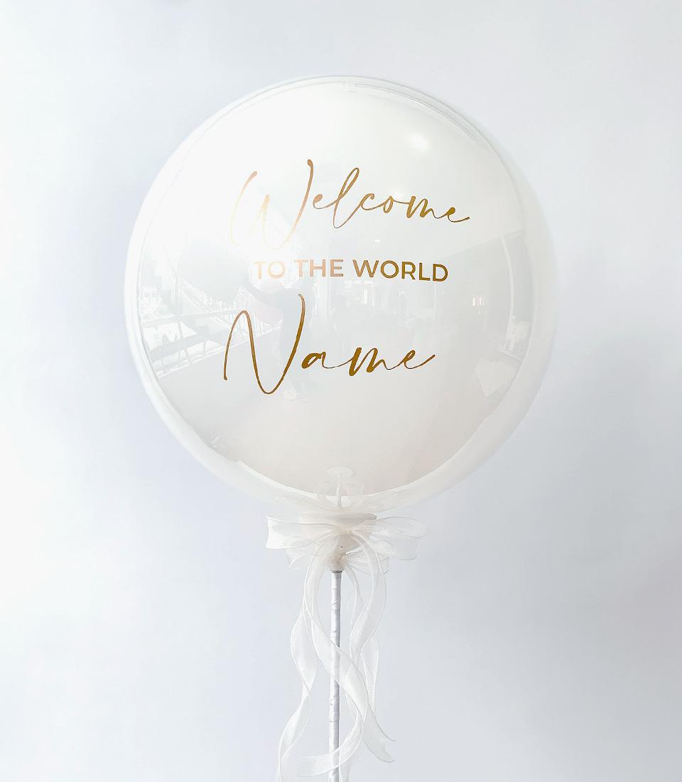 White bubble balloon with gold "Welcome to the World" lettering and flowing white ribbon, new baby gift