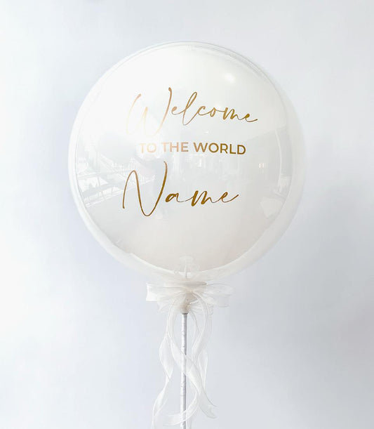 White bubble balloon with gold "Welcome to the World" lettering and flowing white ribbon, new baby gift