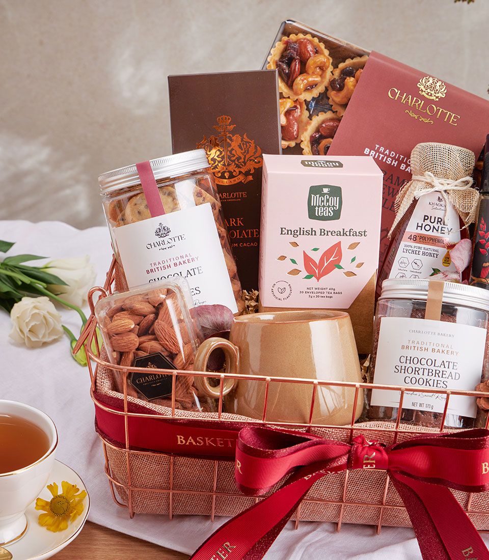 Rose gold wire mesh gift basket with gourmet coffee, cookies, salted caramel nuts, and ceramic mug tied with red ribbon