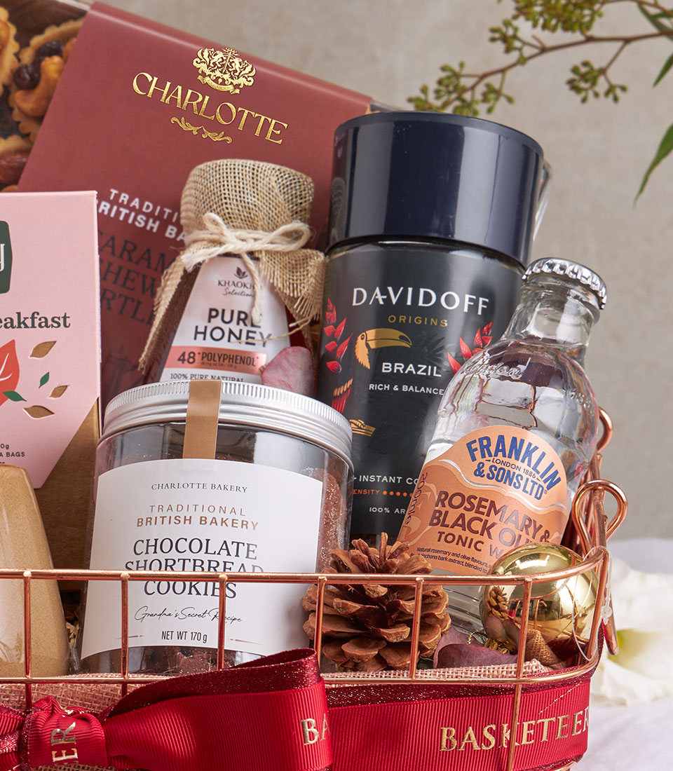 Luxury gourmet hamper with premium coffee, honey, cookies, and tonic water in rose gold wire basket with red ribbon