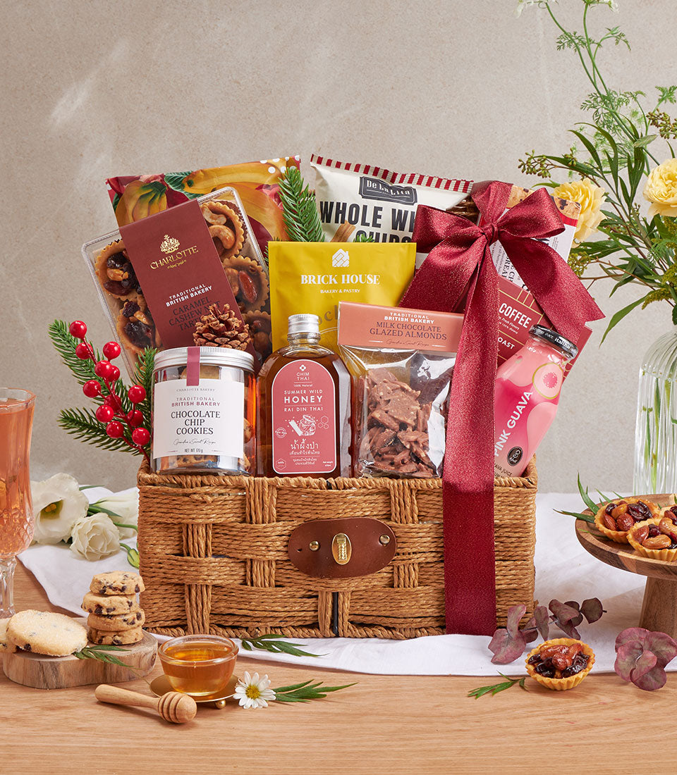 Luxury wicker gift basket with gourmet cookies, tarts, honey, and artisan treats tied with deep red satin ribbon