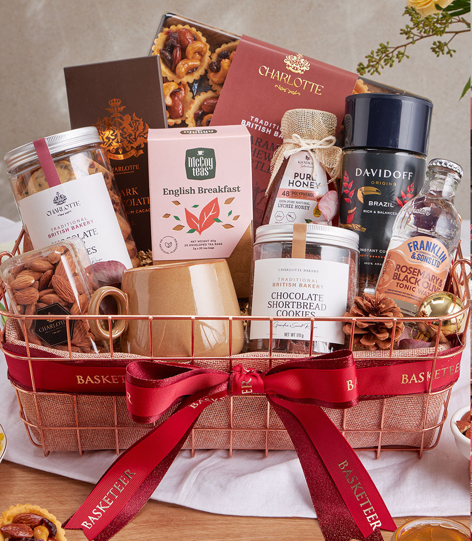 Rose gold wire mesh gift basket with gourmet coffee, cookies, salted caramel nuts, honey and tea, tied with red ribbon