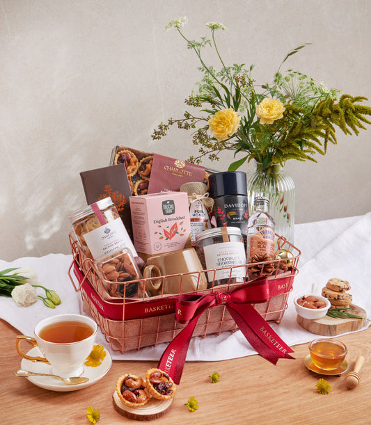 Luxury coffee, cookies and salted caramel nut hamper in rose gold basket with red ribbon, English breakfast tea and honey