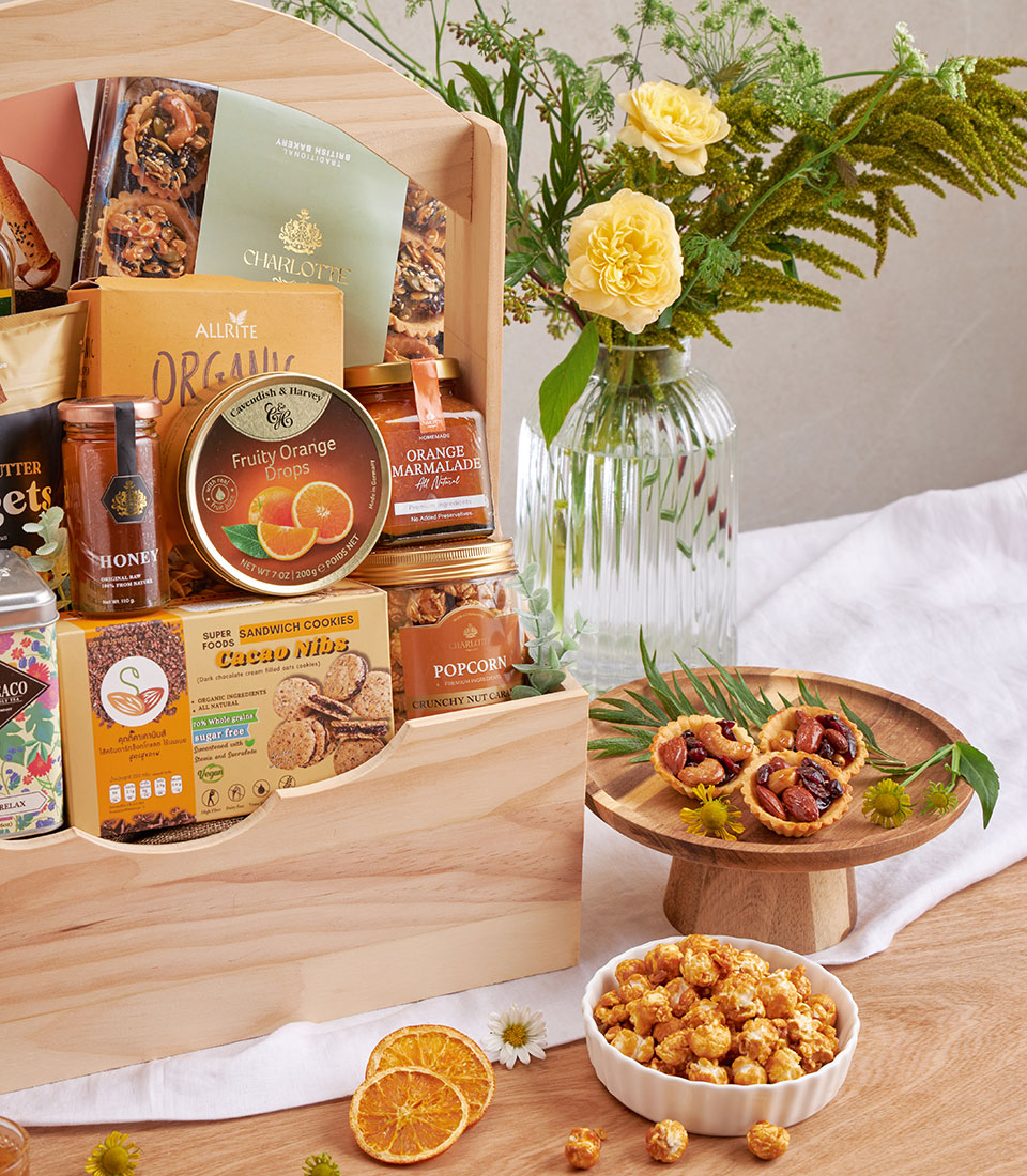 Wooden gourmet hamper with organic cookies, nuts, honey, tea and caramel popcorn, styled with yellow roses and nut tarts