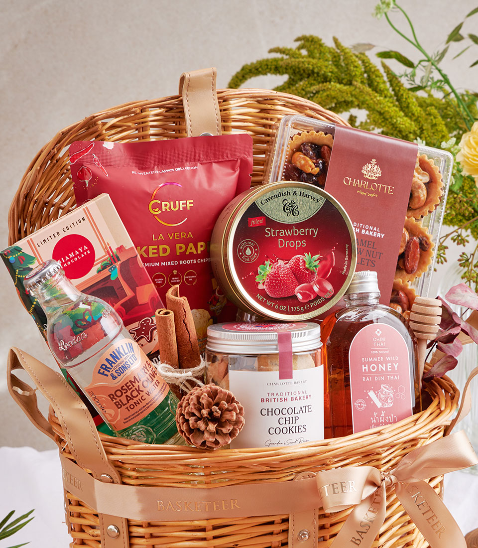 Woven wicker gift basket with chocolate chip cookies, honey, gourmet treats, and festive confections in beige ribbon
