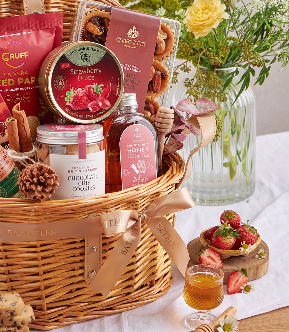 Woven wicker gift basket with honey, chocolate chip cookies, gourmet treats and yellow white flowers