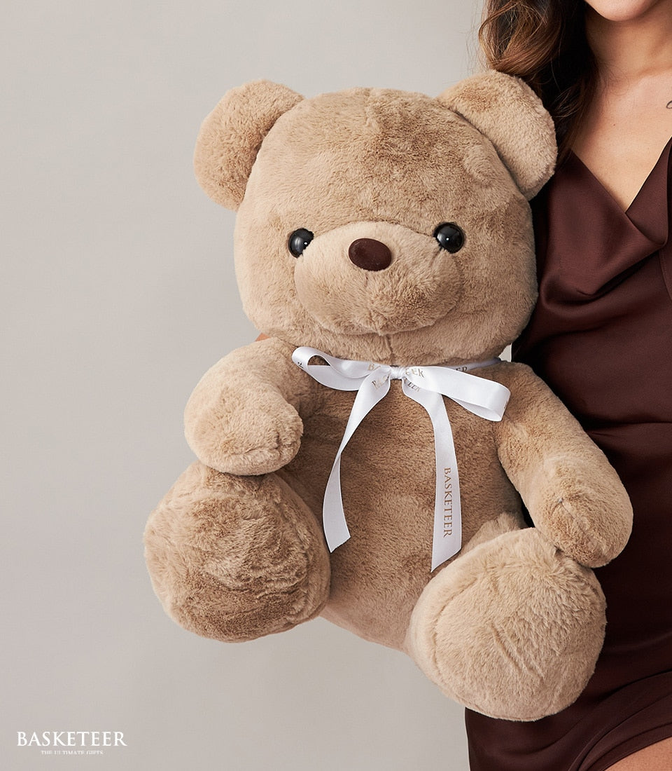 Cream teddy bear with satin bow held for birthday celebration, luxury gift hamper