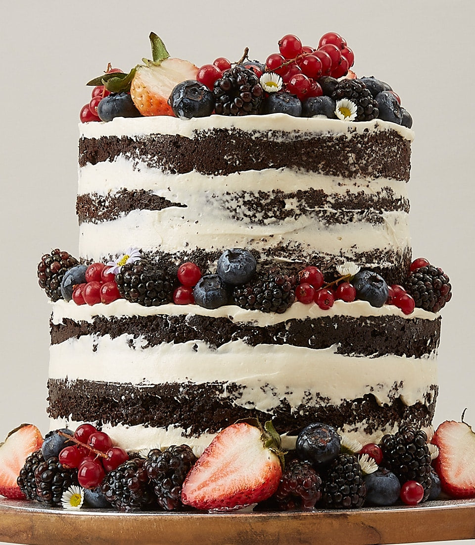Two-tier naked chocolate cake with fresh berries and white frosting for birthday celebrations