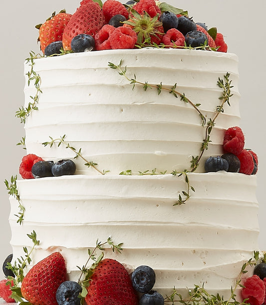 Two-tier white vanilla cake with fresh strawberries, raspberries, and blueberries, artisan celebration cake for birthdays