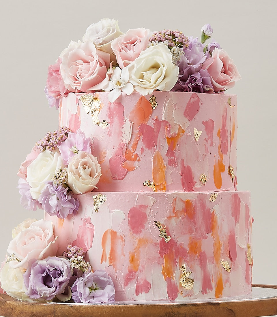 Blush two-tier birthday cake with textured pink frosting, gold leaf, and fresh rose arrangement