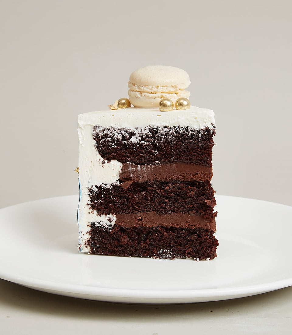 White chocolate layered birthday cake slice with dark ganache and gold macaron decoration