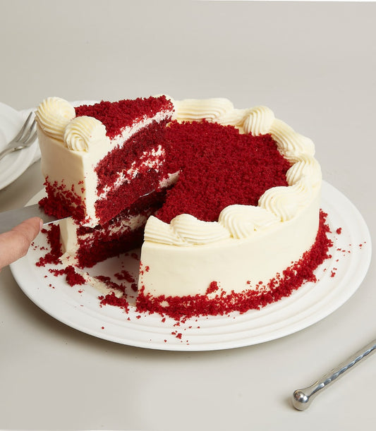 Red velvet birthday cake with cream cheese frosting and piped white swirls, slice being served