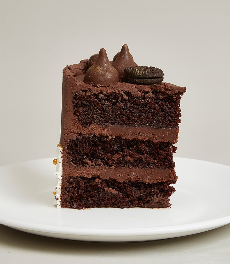 Chocolate-white cream layer cake slice with chocolate frosting, candy kisses, and gold accents