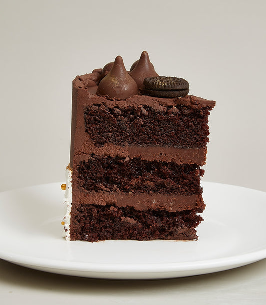 Chocolate-white cream layer cake slice with chocolate frosting, candy kisses, and gold accents