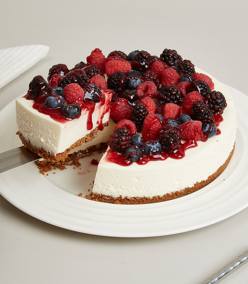 Whole berry cheesecake with graham cracker crust, fresh raspberries, blueberries, and blackberries with berry sauce