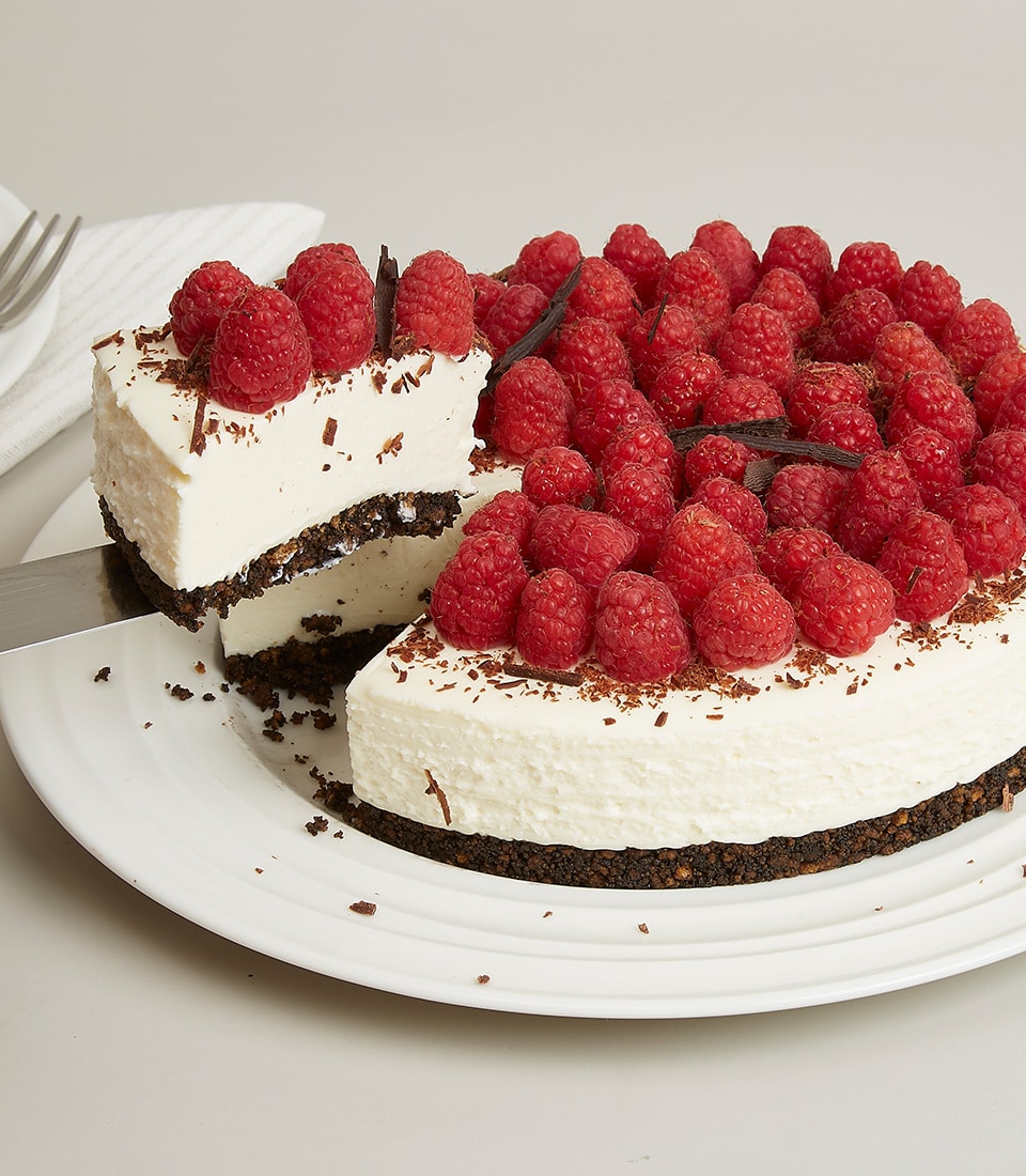 Raspberry cream cheesecake with dark chocolate shavings and fresh berries, served on white plate