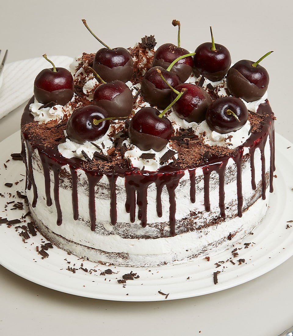 Black Forest cake with dark chocolate layers, cherry glaze, whipped cream, and chocolate shavings on white plate