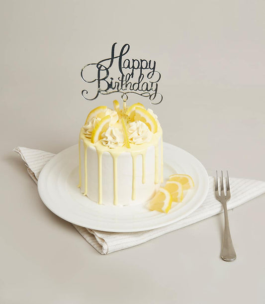 Lemon white cream mini cake with yellow drip glaze, piped frosting, and fresh lemon slices on ceramic plate