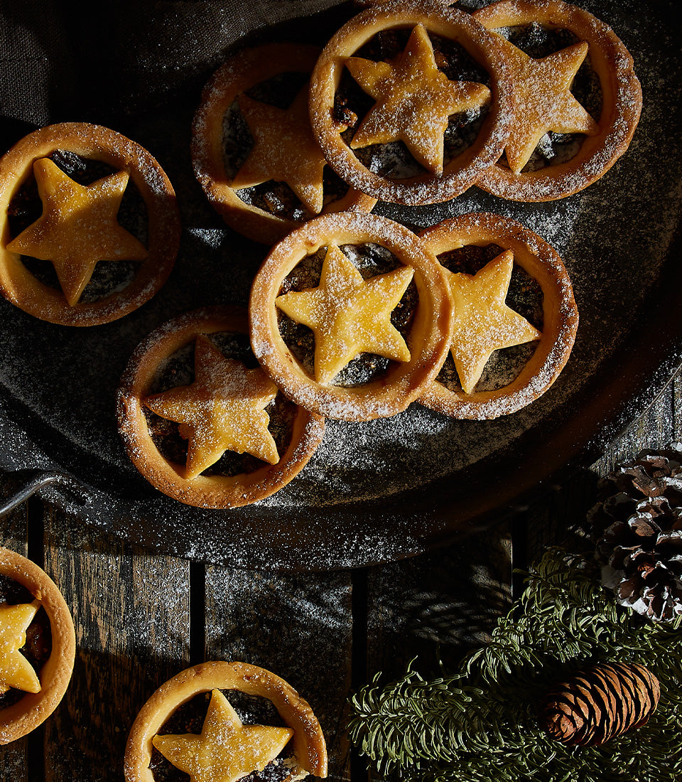 Star-shaped mince pies dusted with powdered sugar, golden pastry with festive evergreen and pinecones on rustic wood