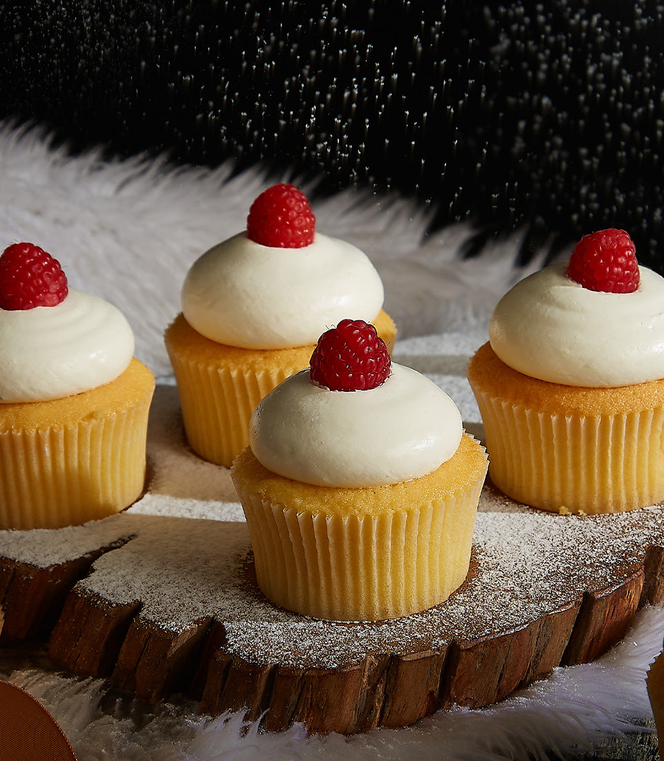 Vanilla cupcakes with white frosting and fresh raspberries on rustic wood, dusted with powdered sugar for Christmas