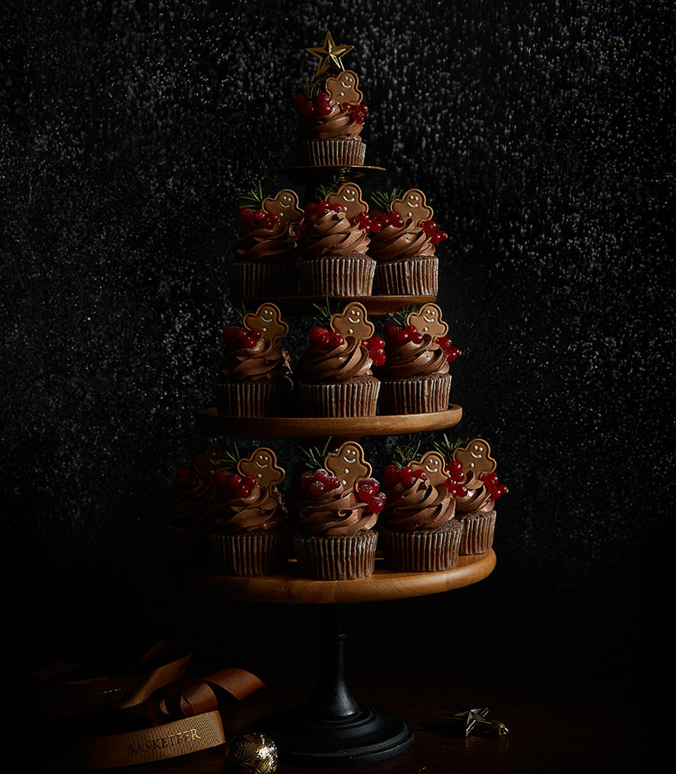 Chocolate ganache gingerbread man cupcakes arranged in Christmas tree shape with red currants and rosemary sprigs