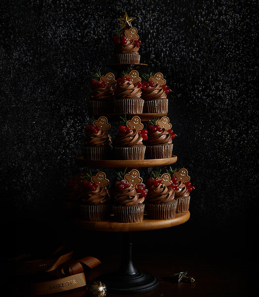 Chocolate ganache gingerbread man cupcakes arranged in Christmas tree shape with red currants and rosemary sprigs
