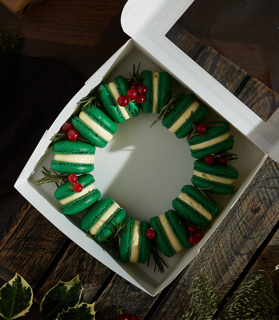 Green brandy butter cream macarons with festive berries and rosemary in holiday wreath gift box