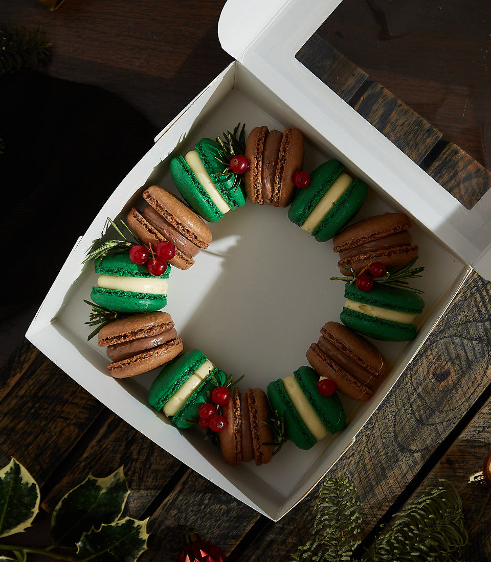 Festive amaretto and brandy cream macarons in green and brown shells with rosemary and red currants, arranged in white gift