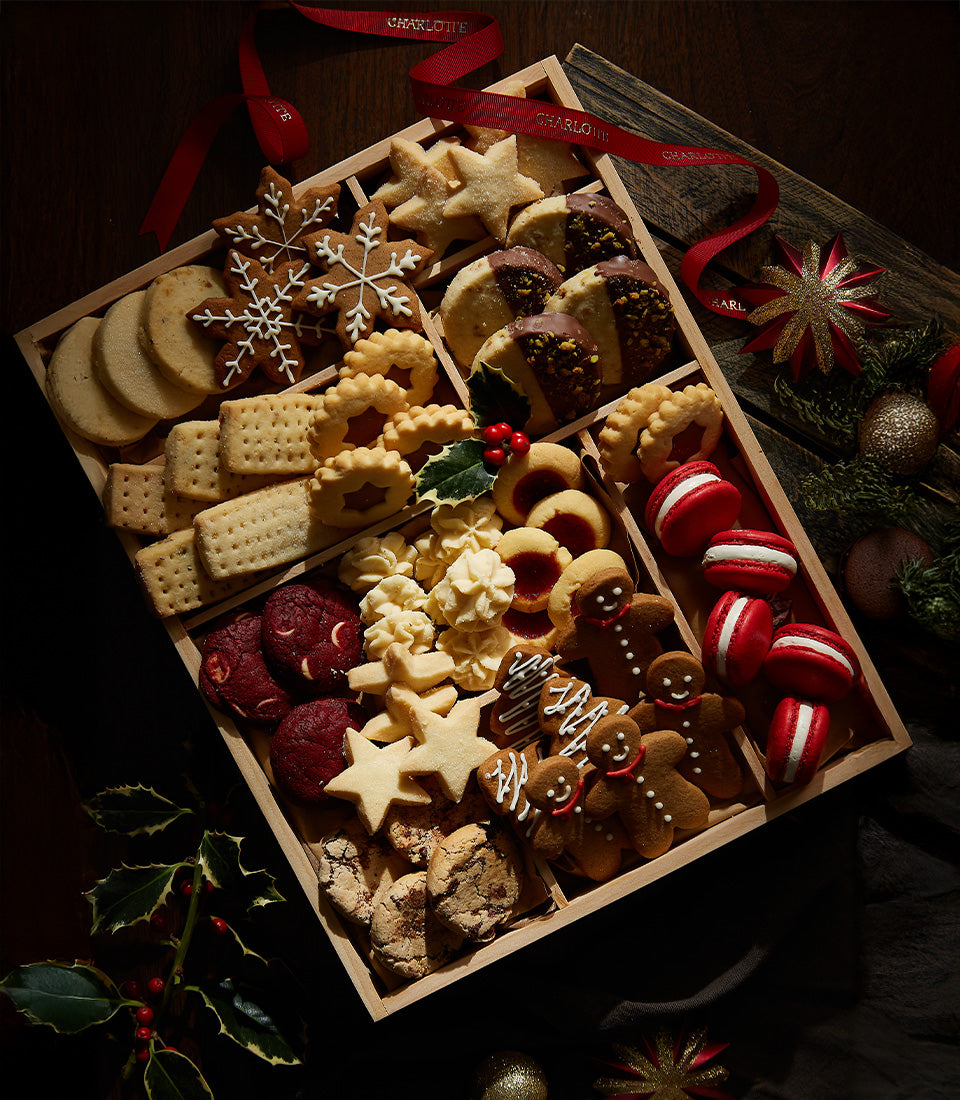 Assorted Christmas cookies and treats in wooden compartment tray with red ribbon, including snowflake and gingerbread shapes