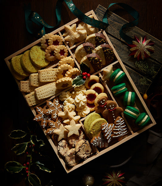 Wooden gift box of assorted Christmas cookies with star shortbread, gingerbread, and macarons, tied with green ribbon