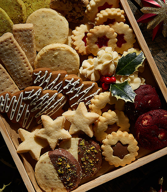 Assorted Christmas cookies and shortbread in wooden tray with gingerbread, jam-filled rounds, and chocolate-pistachio pieces