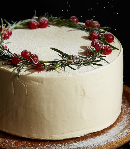Winter Wonderland carrot cake with white frosting, rosemary wreath and sugared cranberries, dusted with powdered sugar