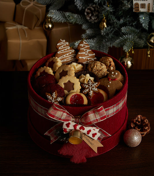 Festive red Christmas cookie box with gingerbread, frosted trees, snowflakes, and shortbread, tied with plaid ribbon and