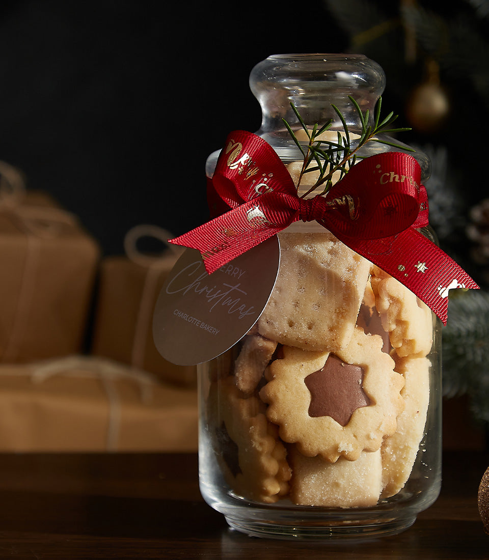Festive cookies jar with shortbread and chocolate star cookies, red ribbon with gold accents and rosemary sprig