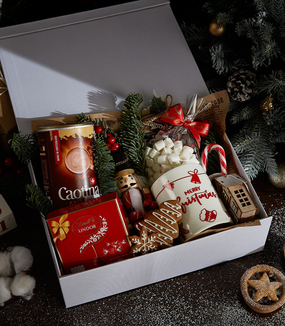 Festive white Christmas gift box with hot chocolate, Lindor chocolates, nutcracker, marshmallows, mug, and gingerbread