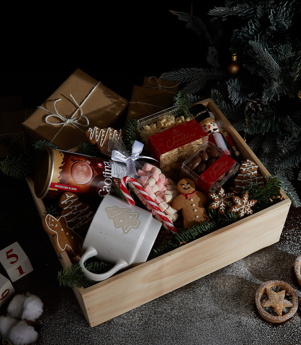 Festive wooden crate with hot chocolate, gingerbread cookies, marshmallows, and Christmas tree mug