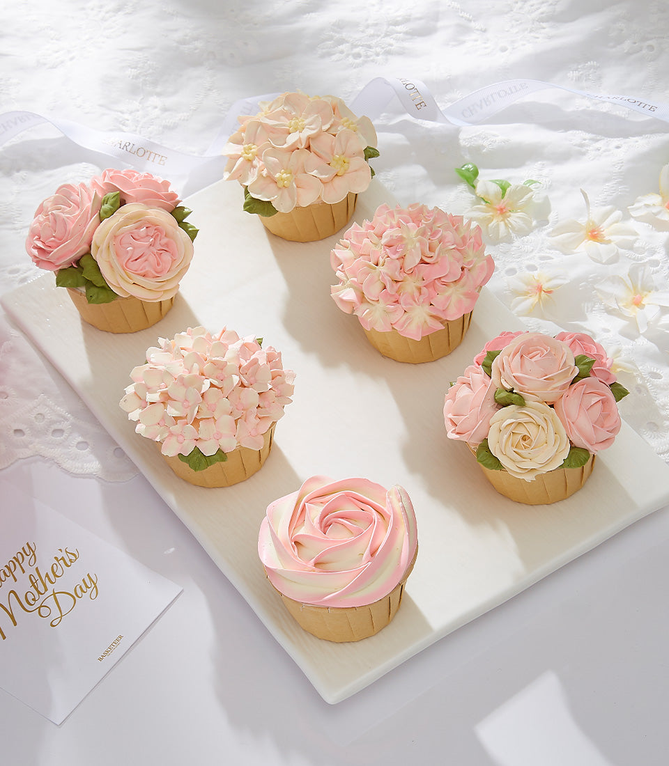 Elaborately decorated Mother's Day cupcakes with pink hydrangea and rose buttercream flowers on white tray