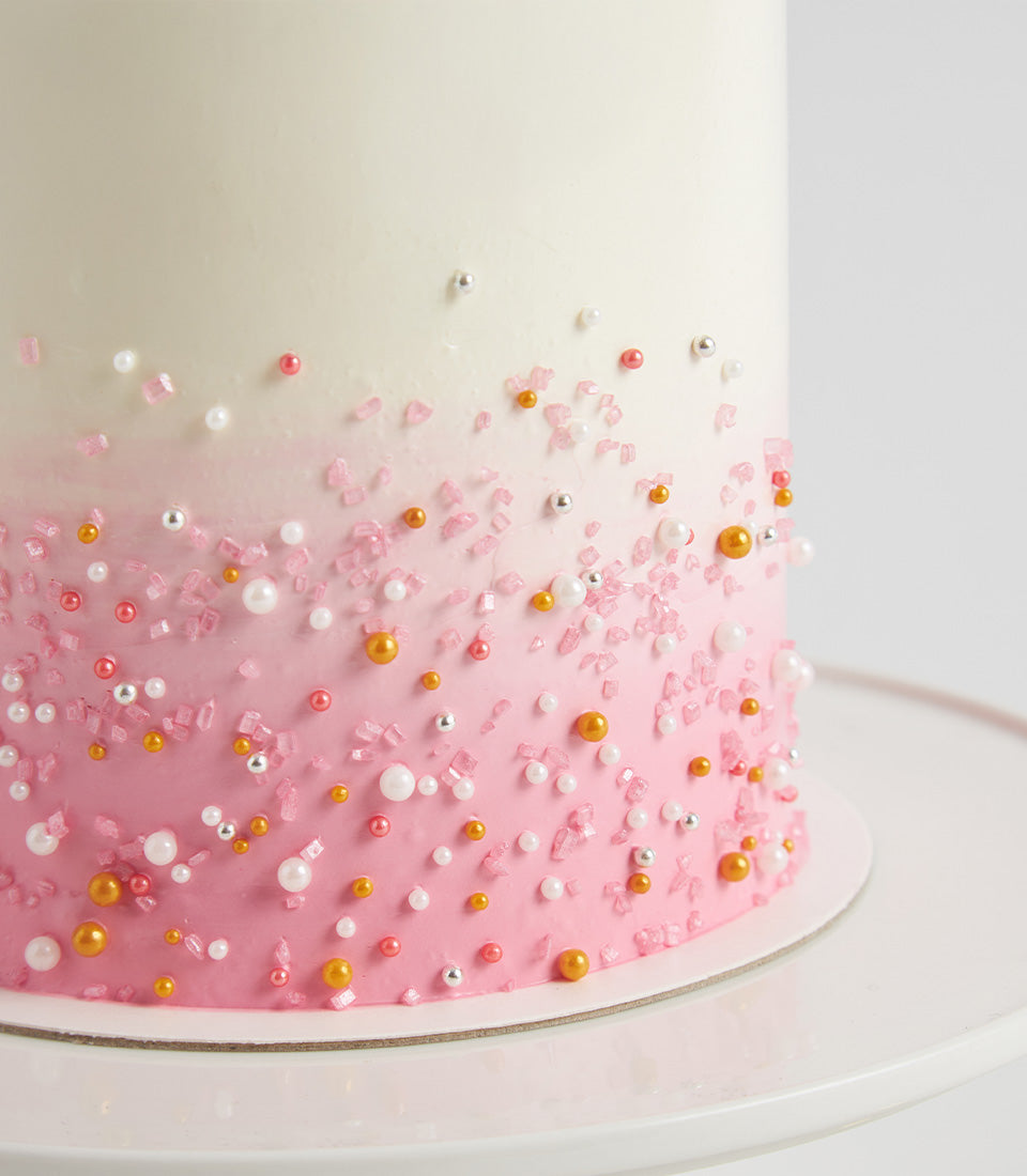 Pink ombré buttercream layer cake with pearl sprinkles and gold sugar crystals for birthday celebrations