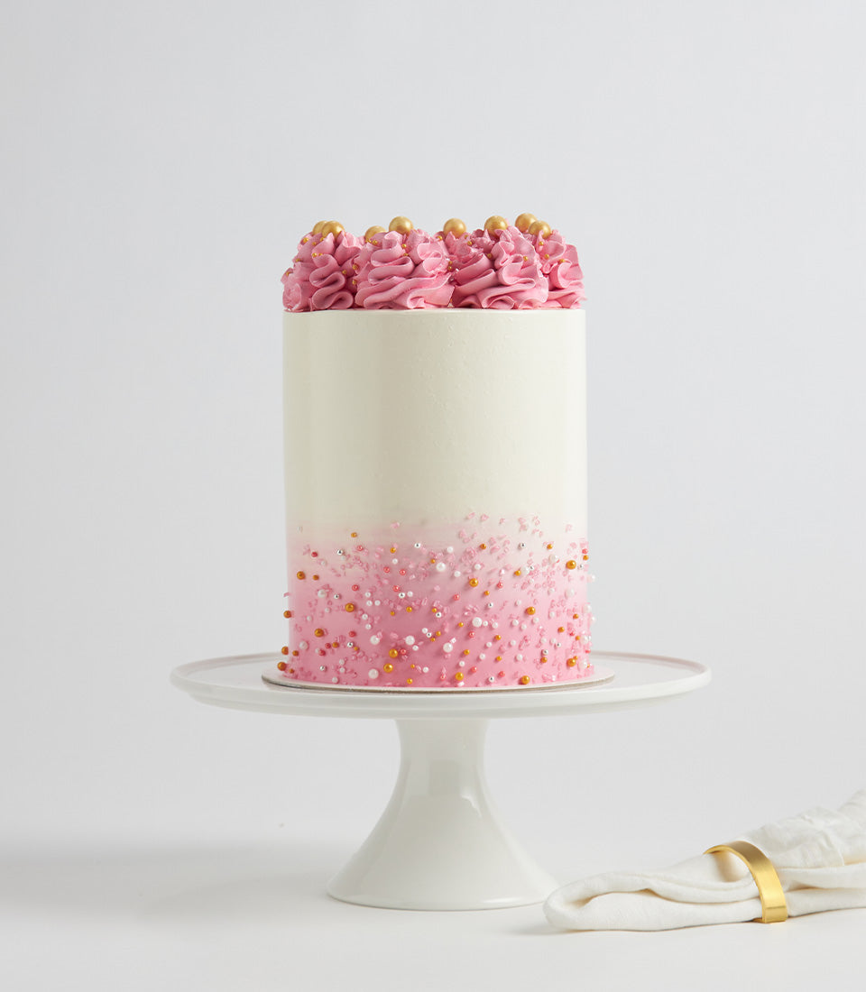Tall pink ombre layer cake with white frosting crown and gold pearl sprinkles, birthday celebration cake from Charlotte