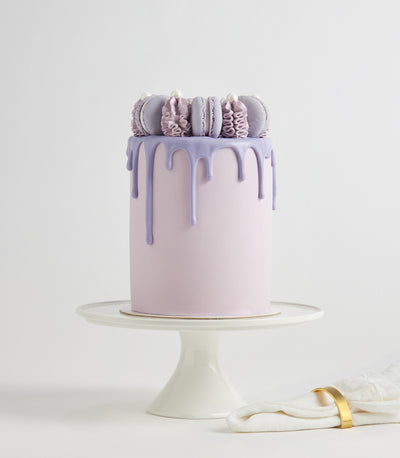 Purple drip macaron layer cake with macarons and pearl details on white cake stand