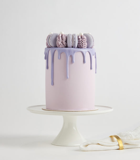 Purple drip macaron layer cake with macarons and pearl details on white cake stand