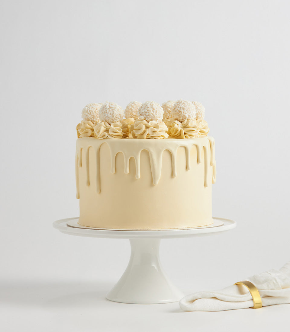 Creamy white chocolate layer cake with pale yellow frosting and coconut pearl decorations, perfect for birthday celebrations