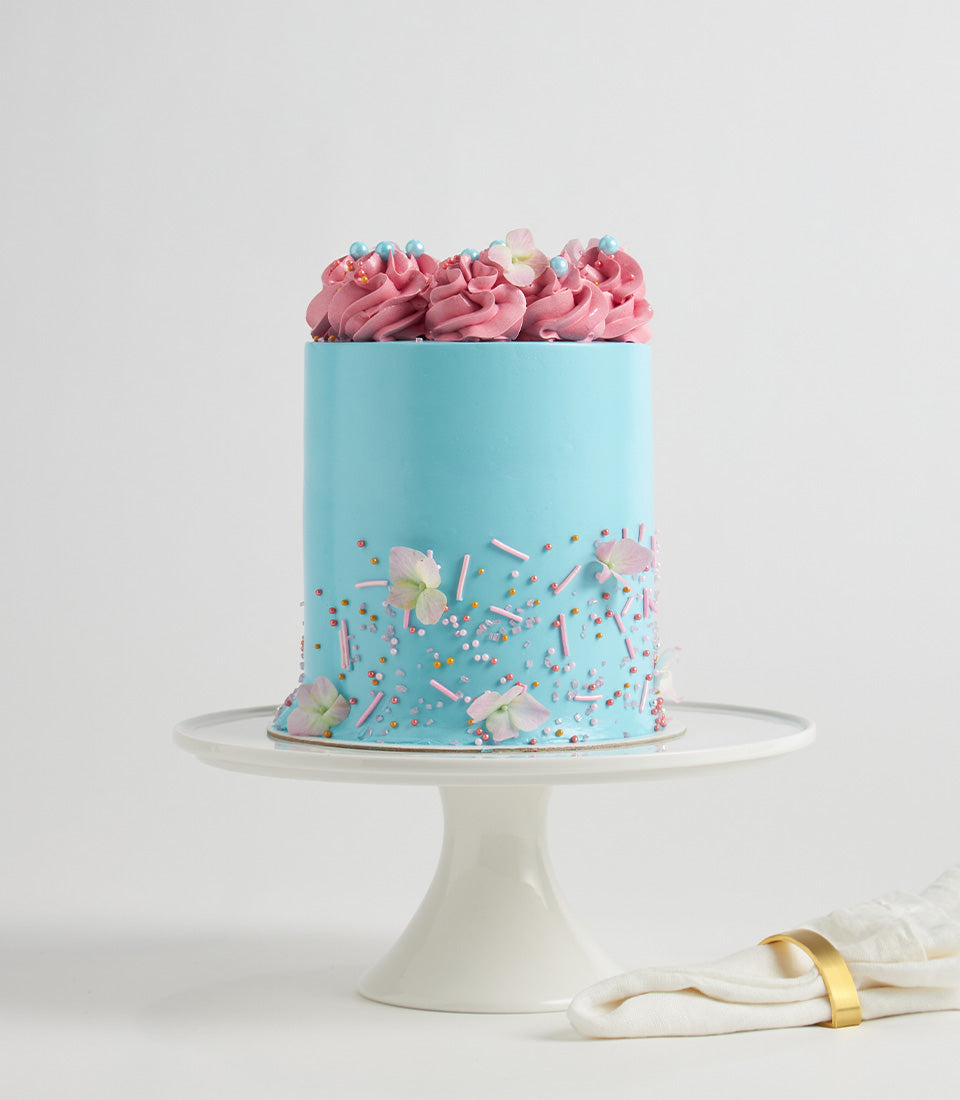 Pastel sky blue and pink layer cake with floral decorations and sprinkles for celebrations