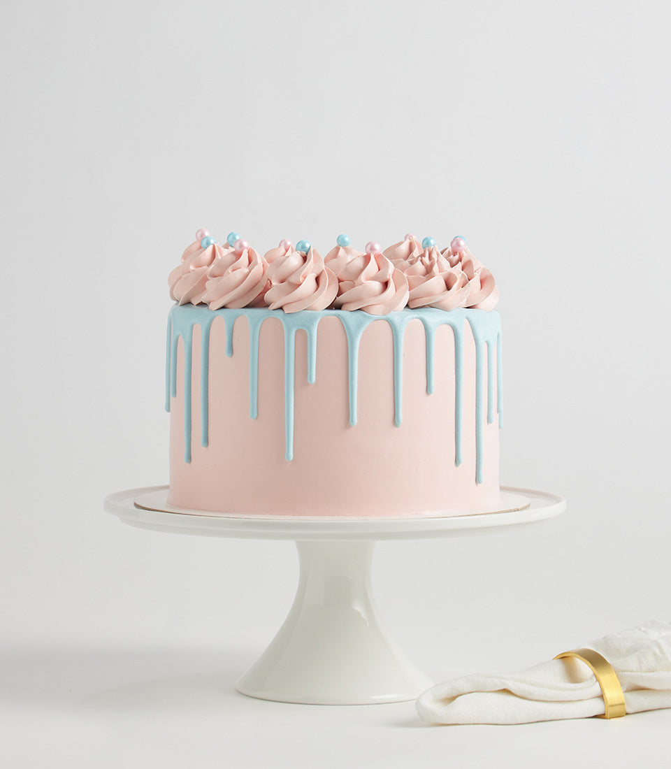 Pastel pink and blue two-layer birthday cake with drip glaze and sprinkled frosting swirls