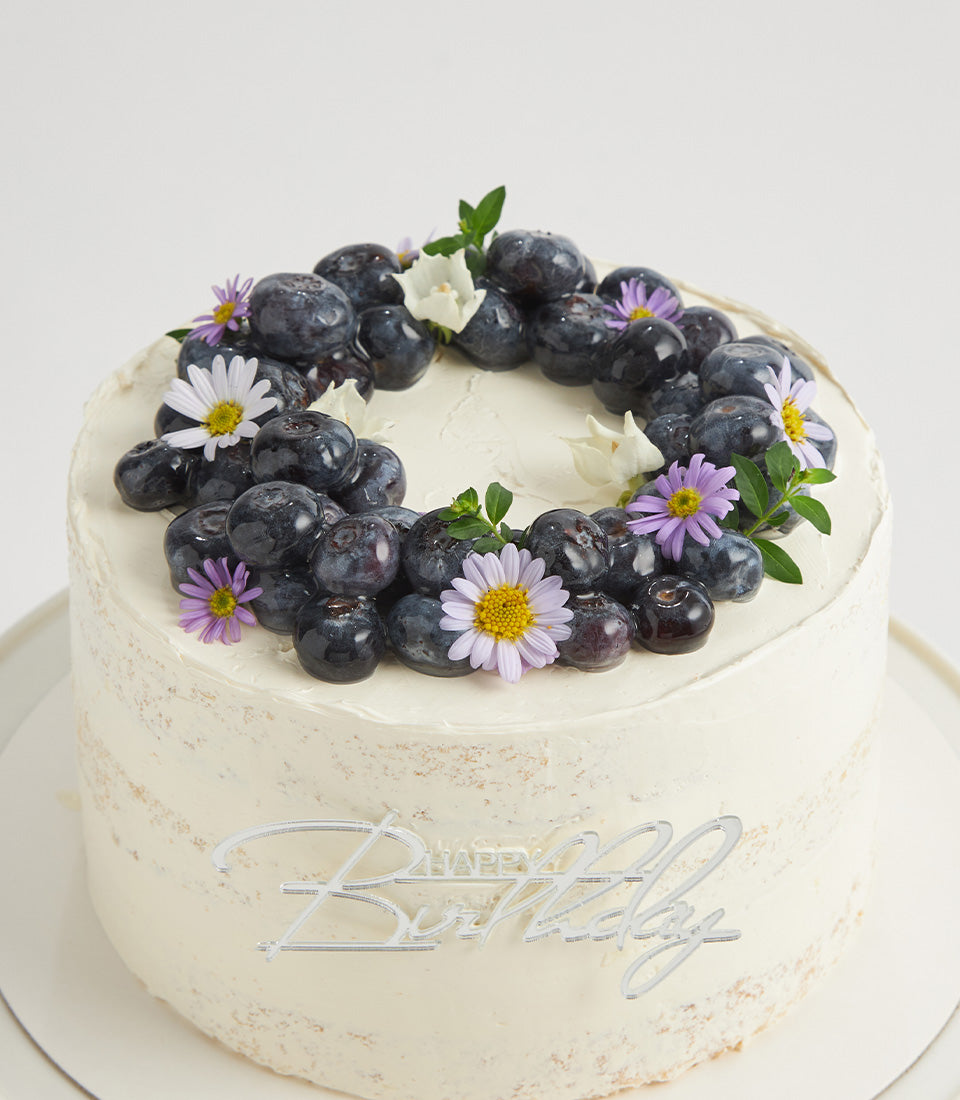 Elegant white naked cake with fresh blueberries, daisies, and Happy Birthday topper